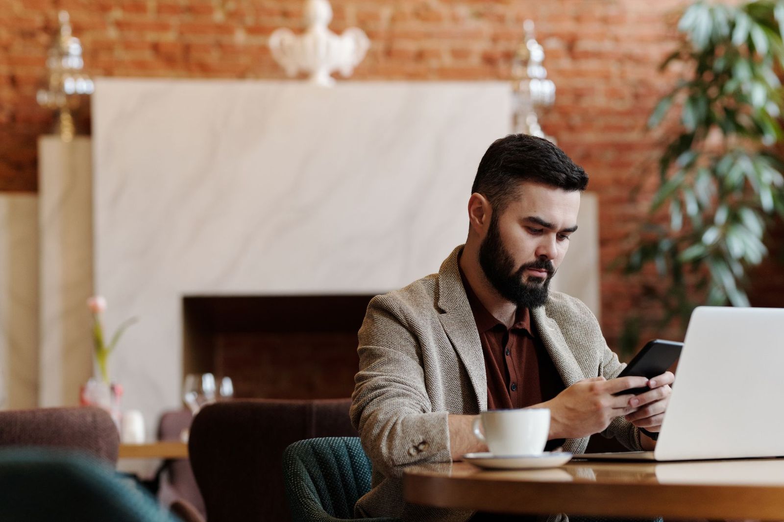 A person researching across a phone and a laptop in a café, the kind of considered, in-the-moment decision now happening inside AI assistants.