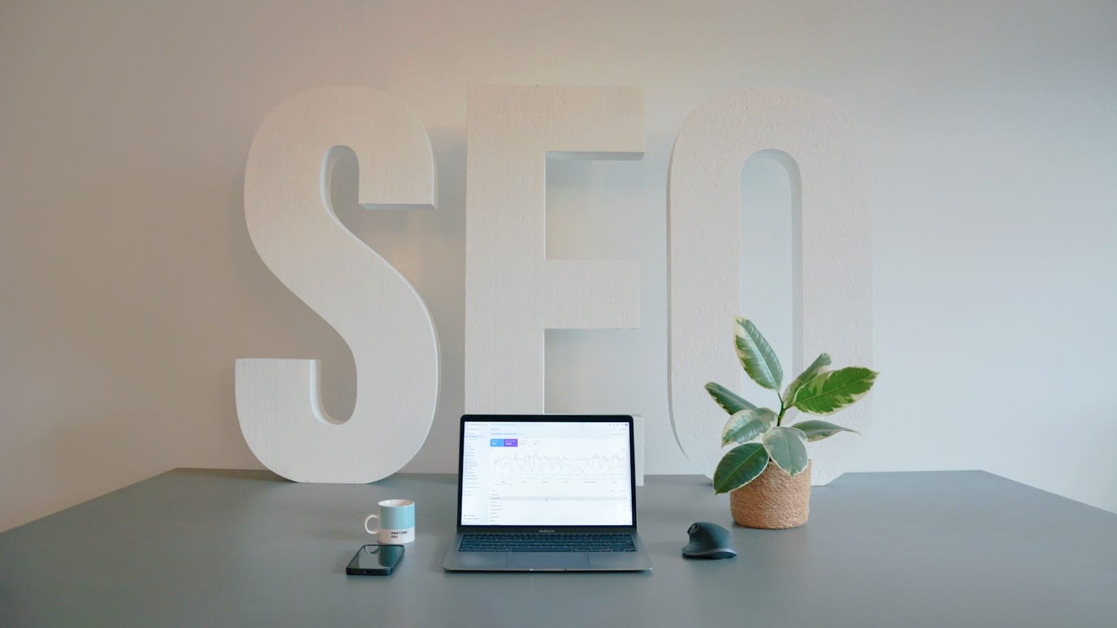 A desk with a laptop and large SEO lettering behind it.