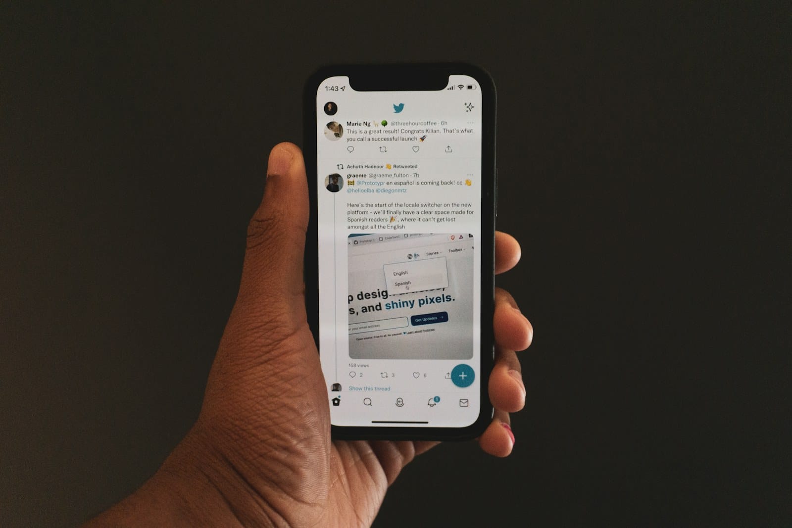 A hand holding a phone with the X (Twitter) feed open.