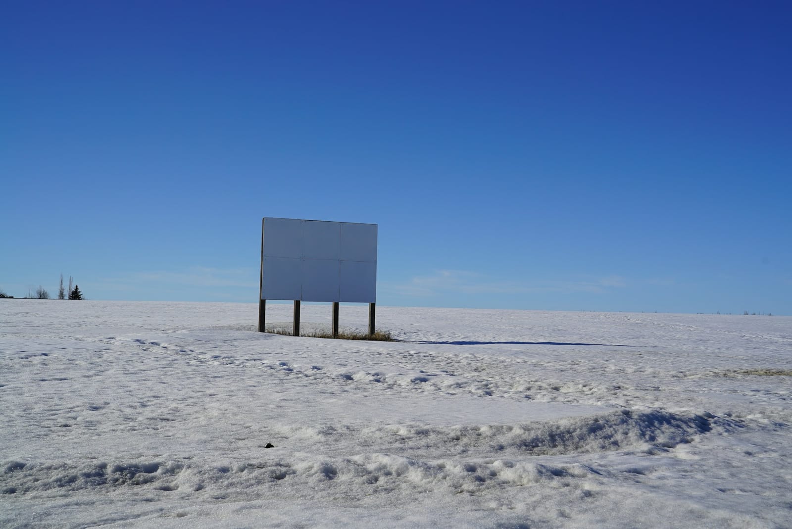 A blank billboard standing alone in an empty snow-covered field.